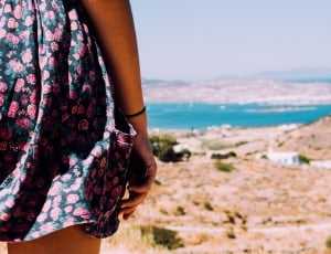 person wearing black and red floral skirt standing on hill looking through the see thumbnail