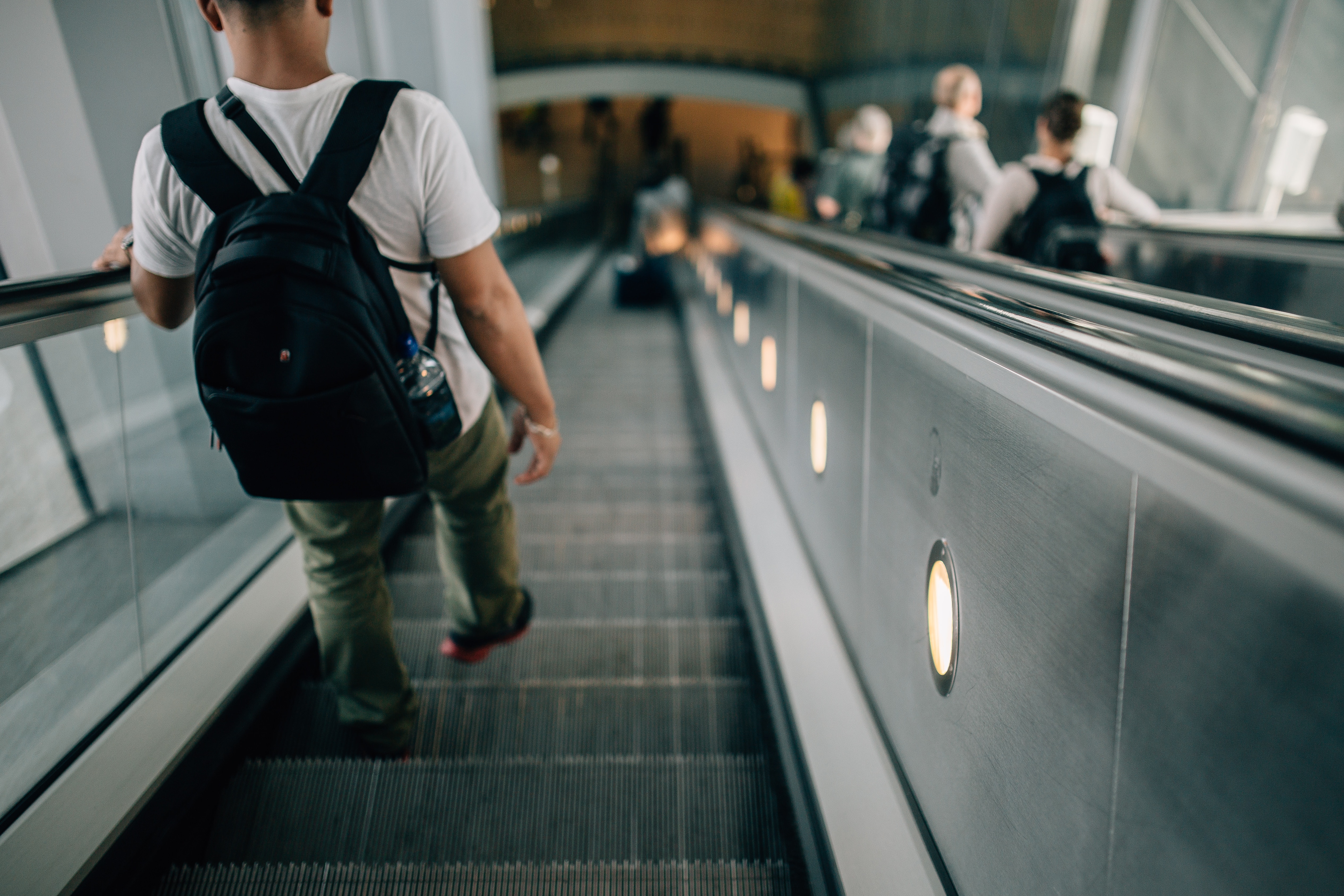 man wearing white shirt and black backpack walking down on escalator