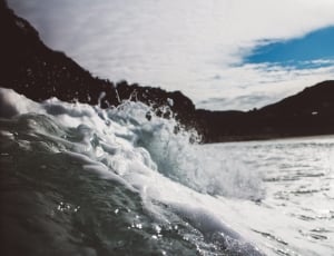 sea waves beside island under white and blue sky thumbnail
