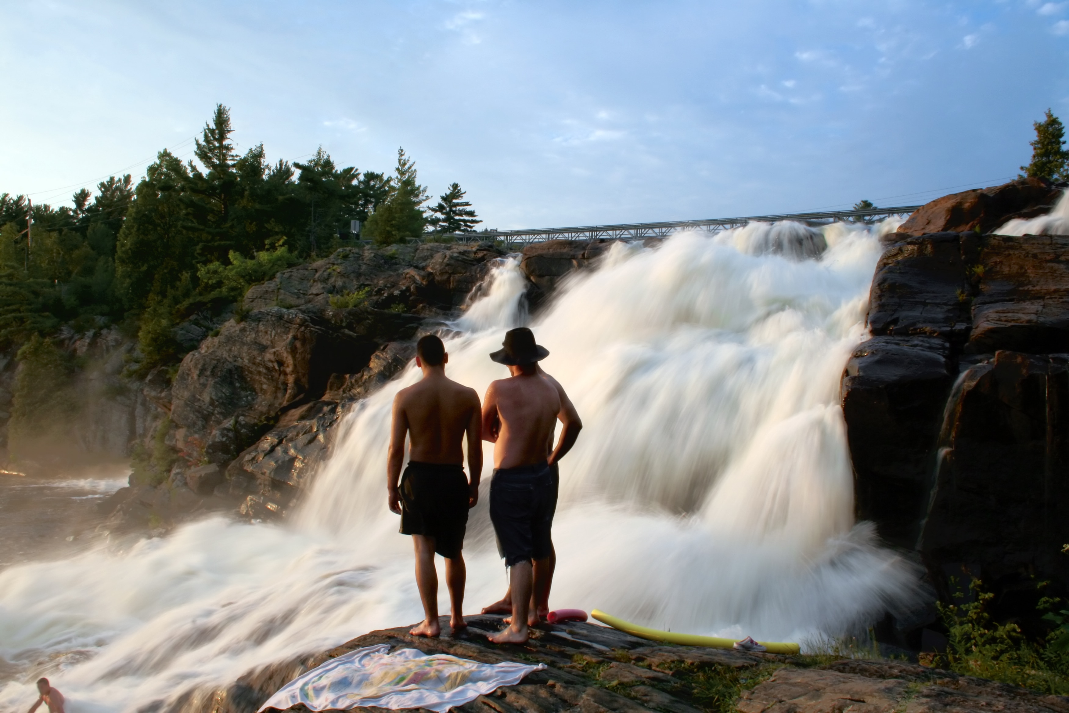 3 person standing near waterfalls during daytime