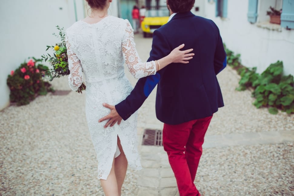 man in blue formal suit jacket and red pants outfit beside woman in white floral long sleeve outfit during daytime preview