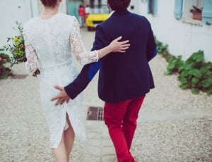 man in blue formal suit jacket and red pants outfit beside woman in white floral long sleeve outfit during daytime thumbnail