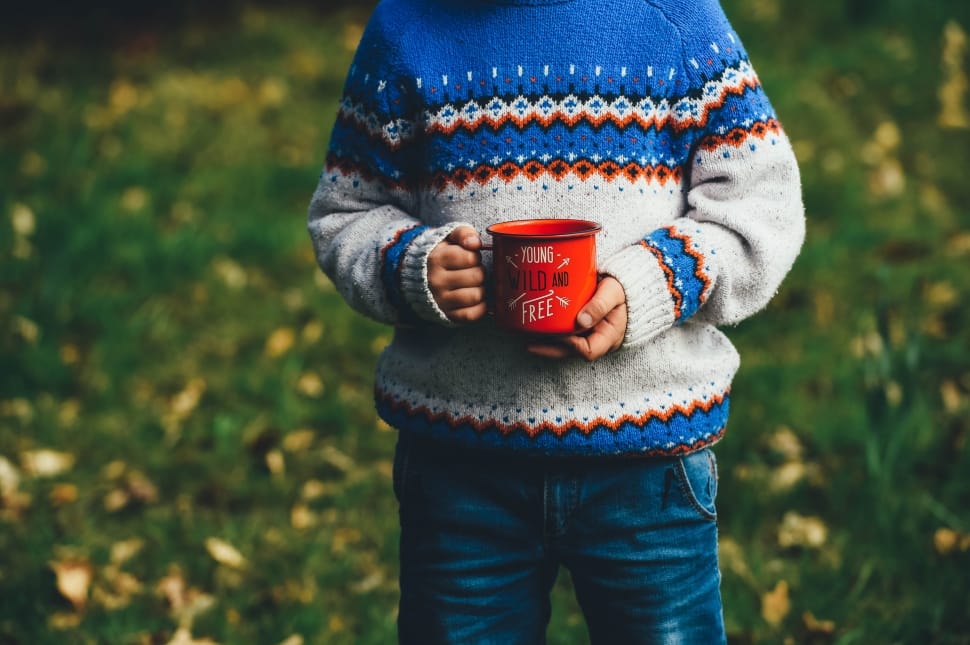 boy wearing orange, white and blue knit sweater holding red mug preview