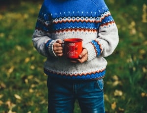 boy wearing orange, white and blue knit sweater holding red mug thumbnail