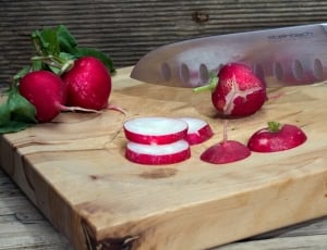 red fruit sliced on brown wooden cutting board with stainless steel kitchen knife thumbnail