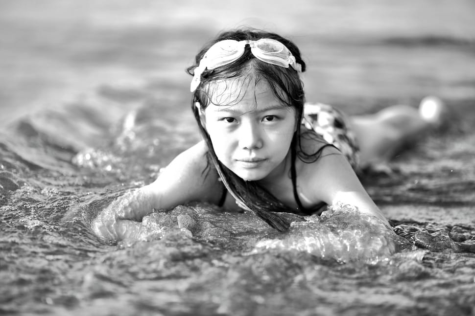 girl with swimming goggles laying on beach shore preview