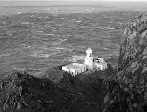 grayscale photography of lighthouse tower beside sea thumbnail