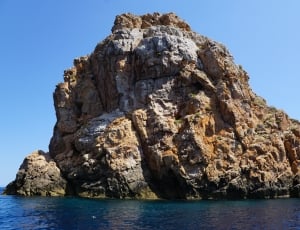 brown boulder on ocean under blue sky during daytime thumbnail