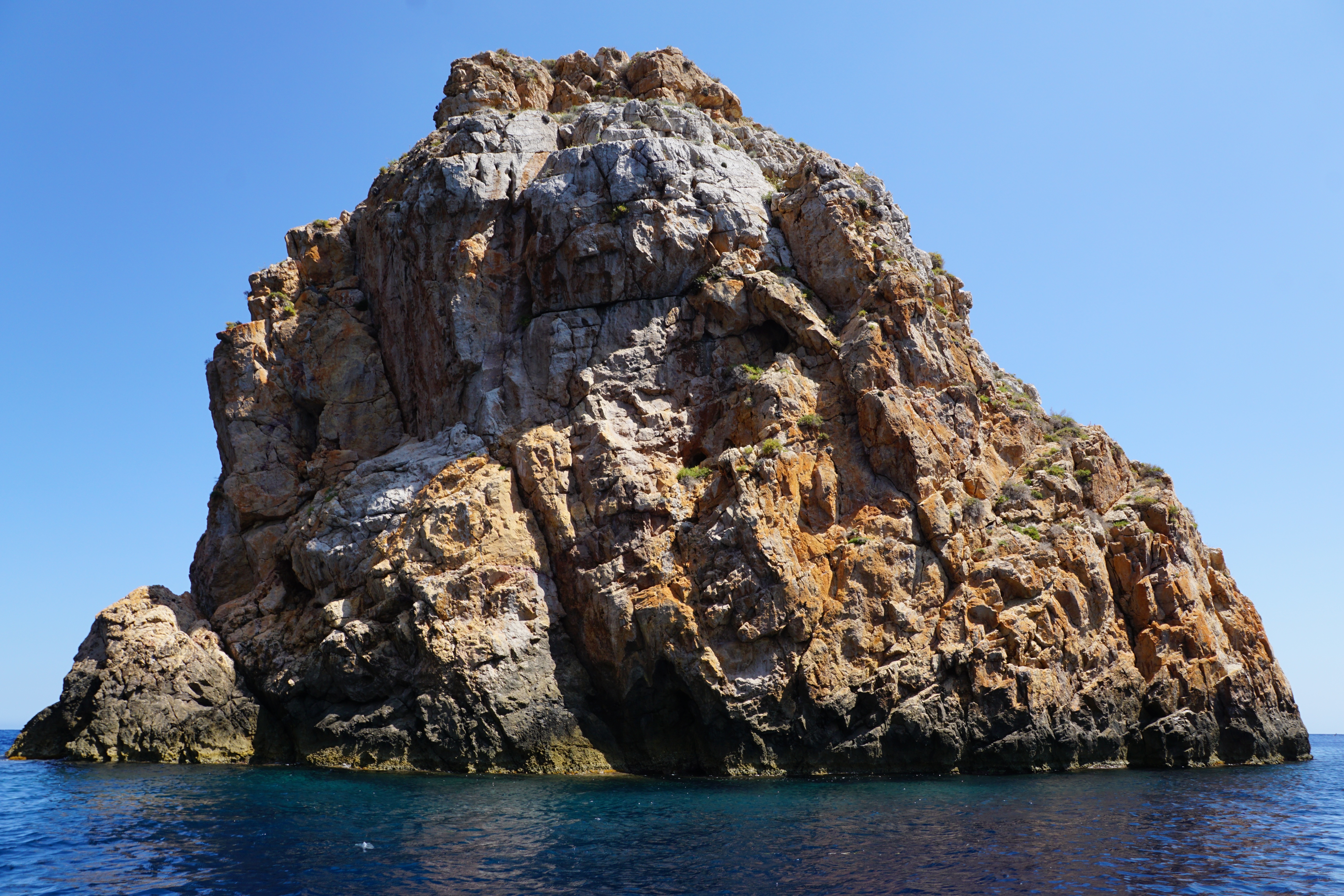 brown boulder on ocean under blue sky during daytime