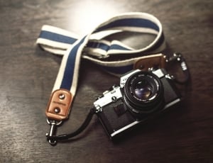 black mini camera with lanyard on top of wooden surface thumbnail