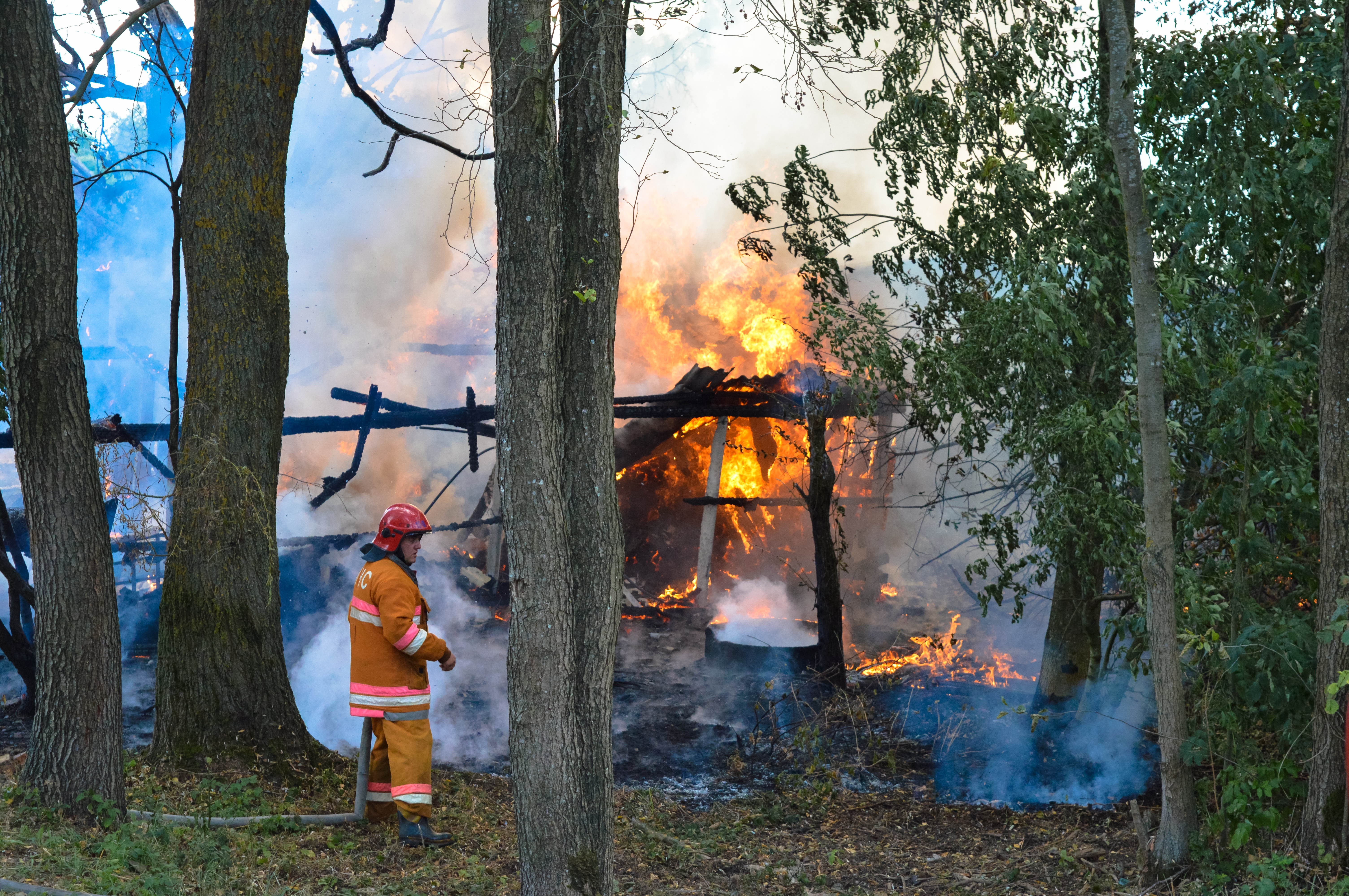 house on fire on a forested area with a fireman