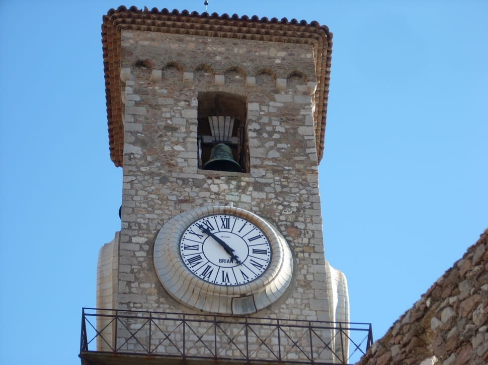 white analog clock mounted on concrete tower with bell on top preview