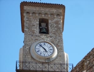 white analog clock mounted on concrete tower with bell on top thumbnail