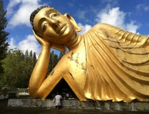 person standing in front of gold buddha near trees during daytime thumbnail