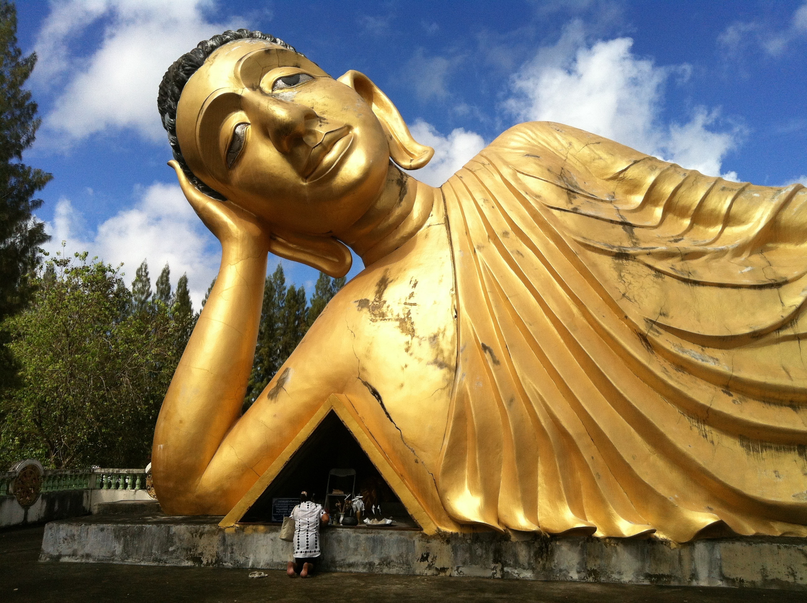 person standing in front of gold buddha near trees during daytime