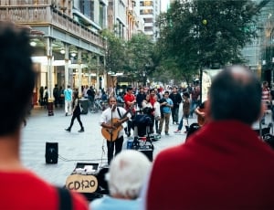 man wearing white shirt and playing guitar surrounded by people during daytime thumbnail