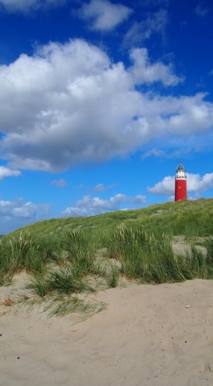 red and white light house near grass field under blue sunny cloudy sky thumbnail