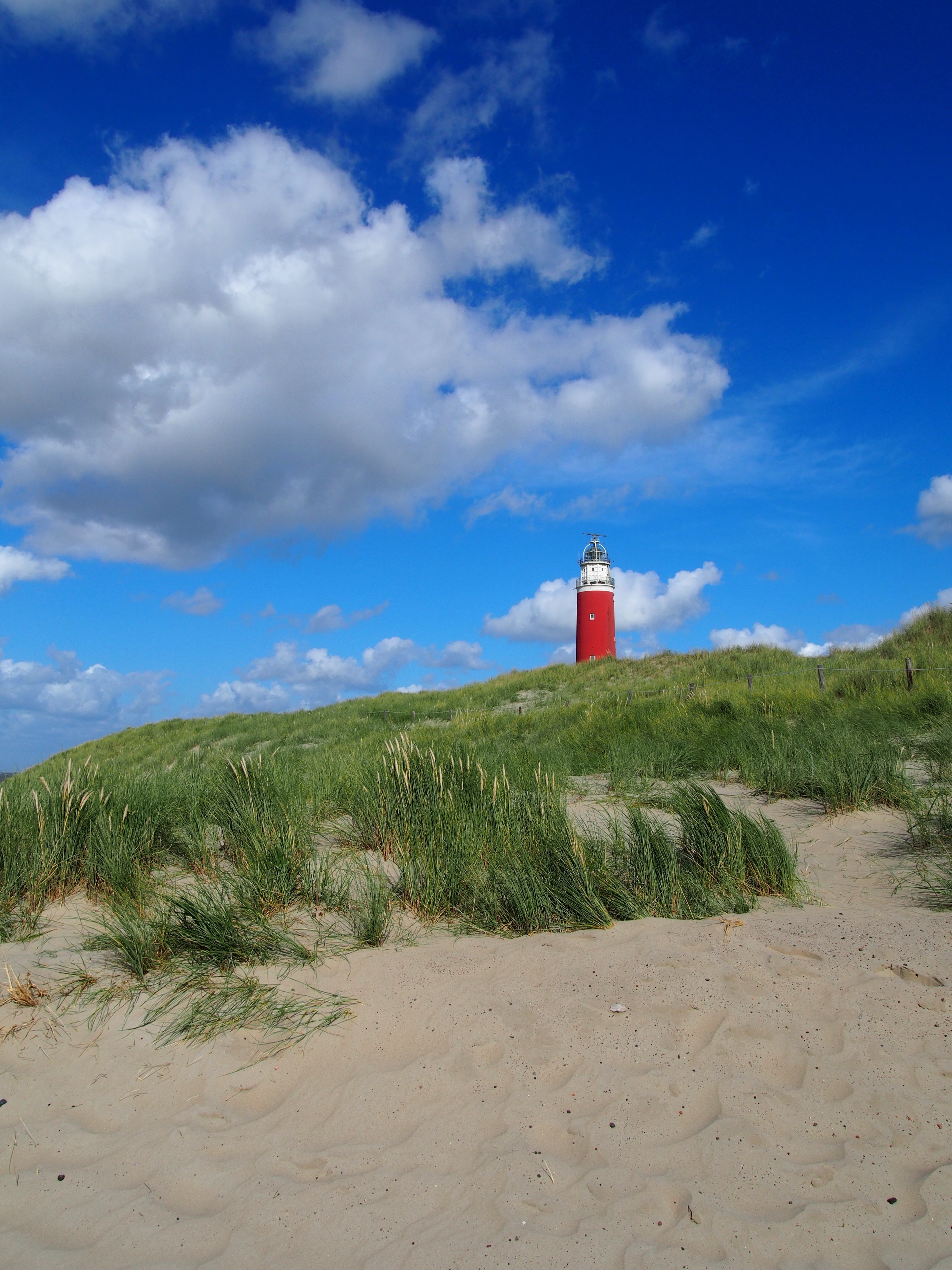 red and white light house near grass field under blue sunny cloudy sky
