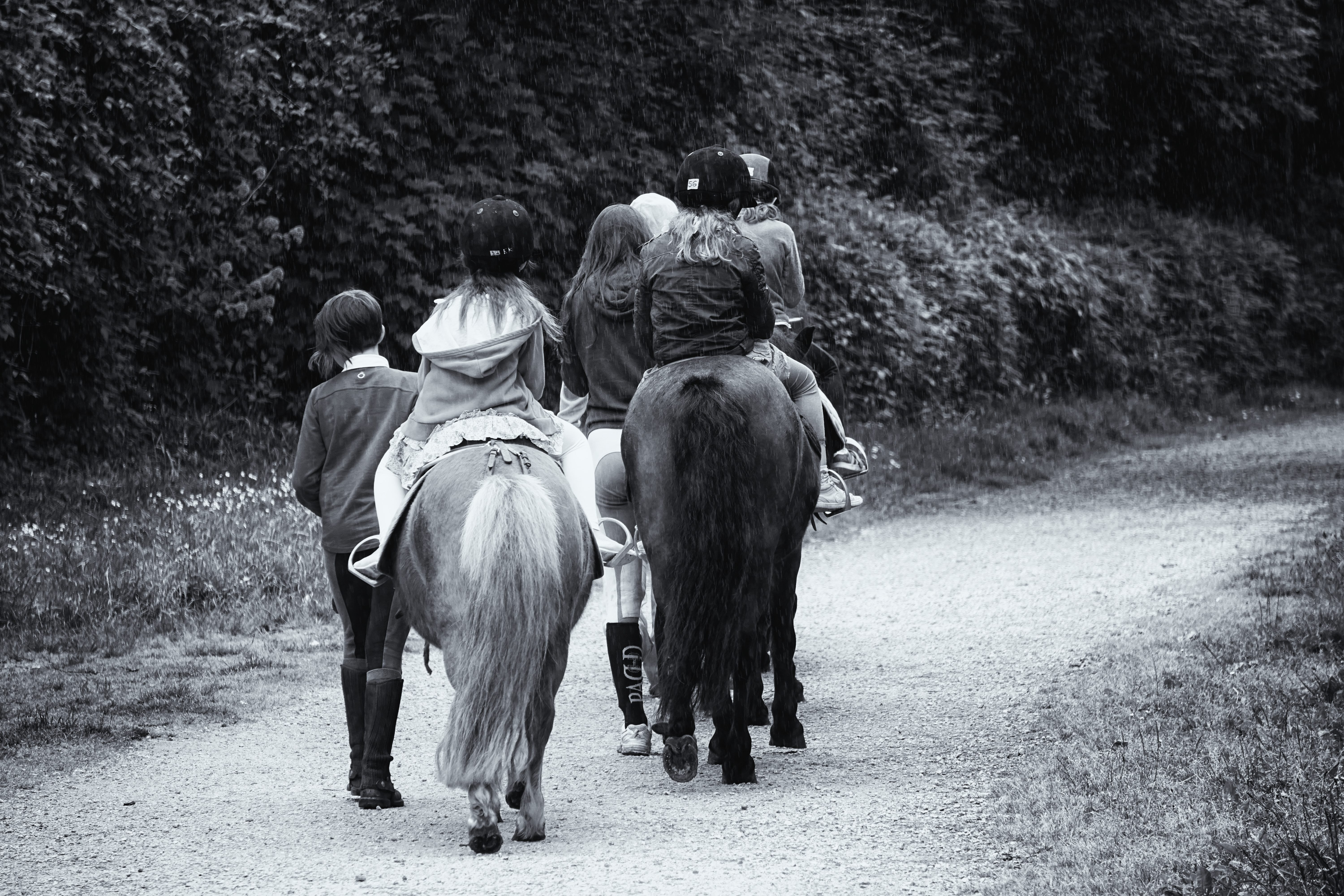 childrens riding on horses grayscale photo