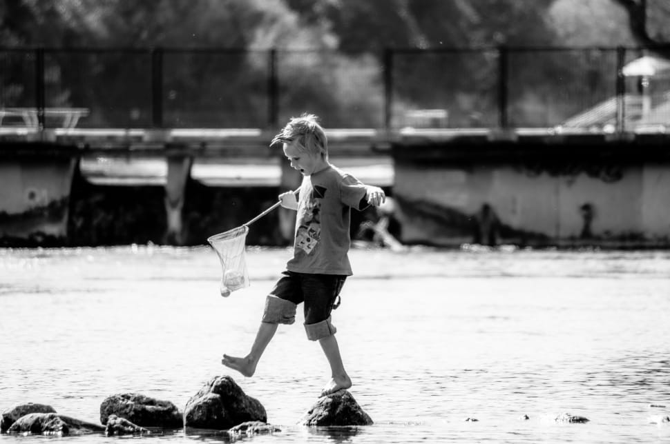 grayscale photo of kid above the water playing holding a net preview