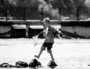 grayscale photo of kid above the water playing holding a net thumbnail