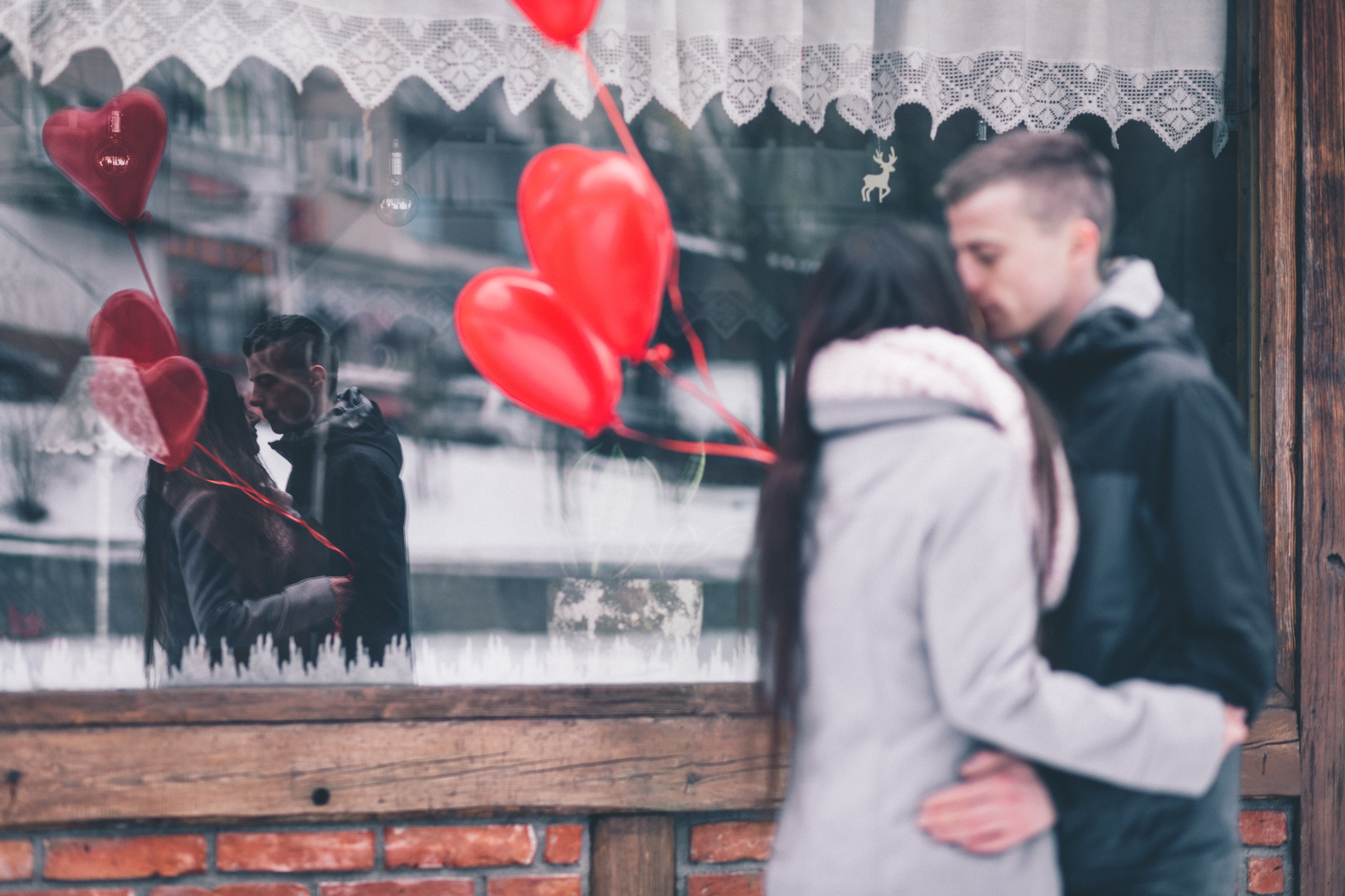 man in black hoodie kissing woman in grey hoodie in front of store