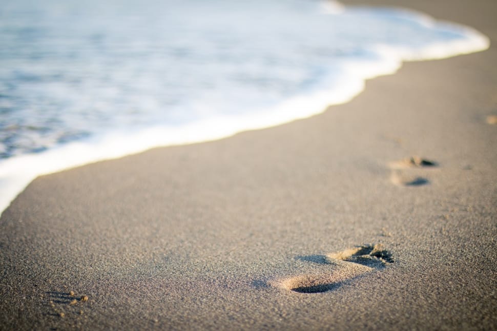 a picture of brown sand and body of water with foot prints preview