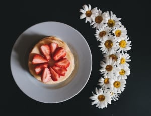 pancake topped with strawberry slices on white ceramic plate near bunch of white flowers thumbnail