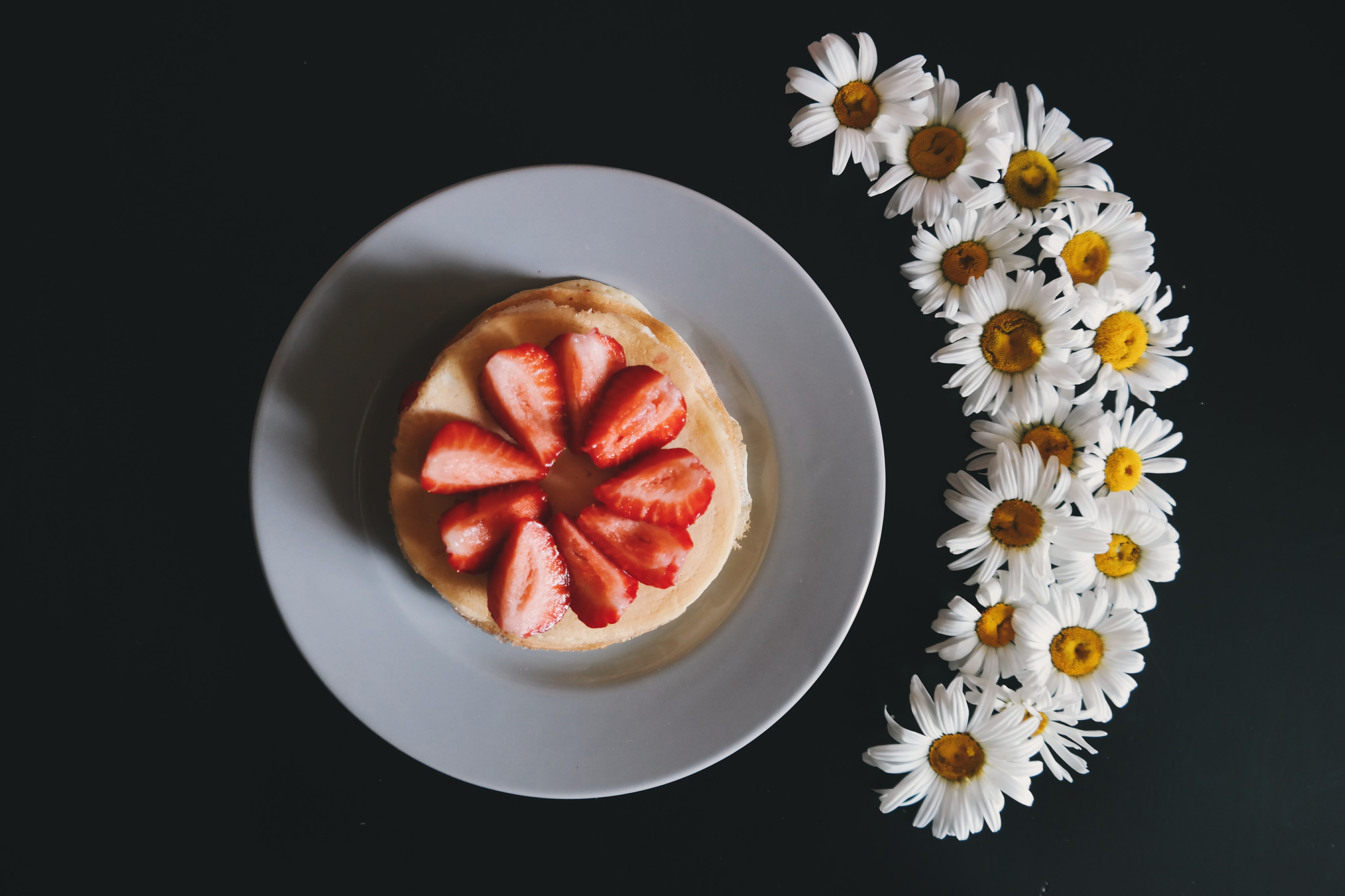 pancake topped with strawberry slices on white ceramic plate near bunch of white flowers
