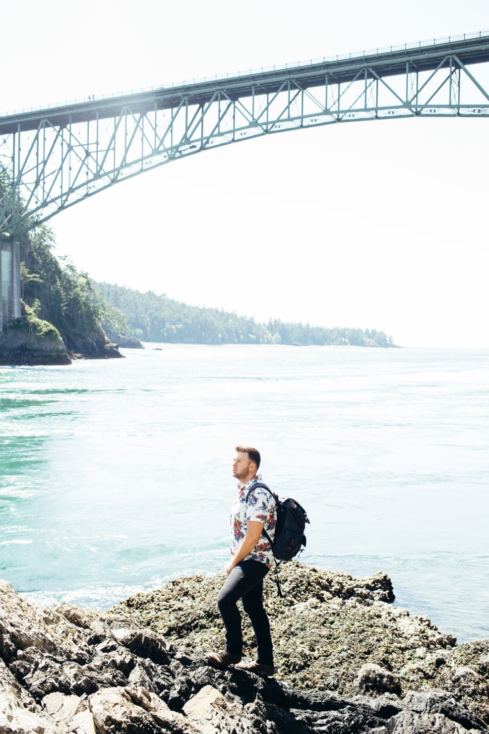 man with black backpack with bridge above him preview