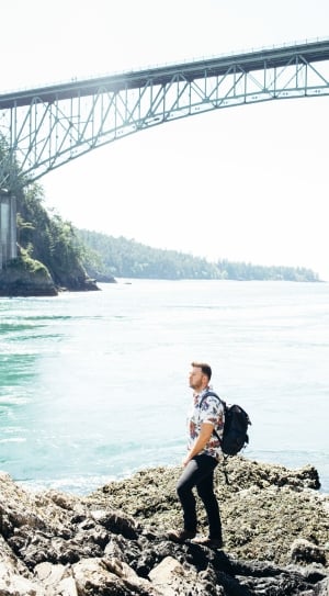 man with black backpack with bridge above him thumbnail