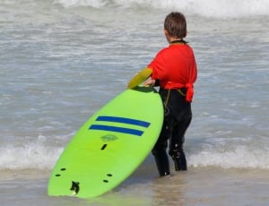 boy holding a green surfboard toward the waves thumbnail