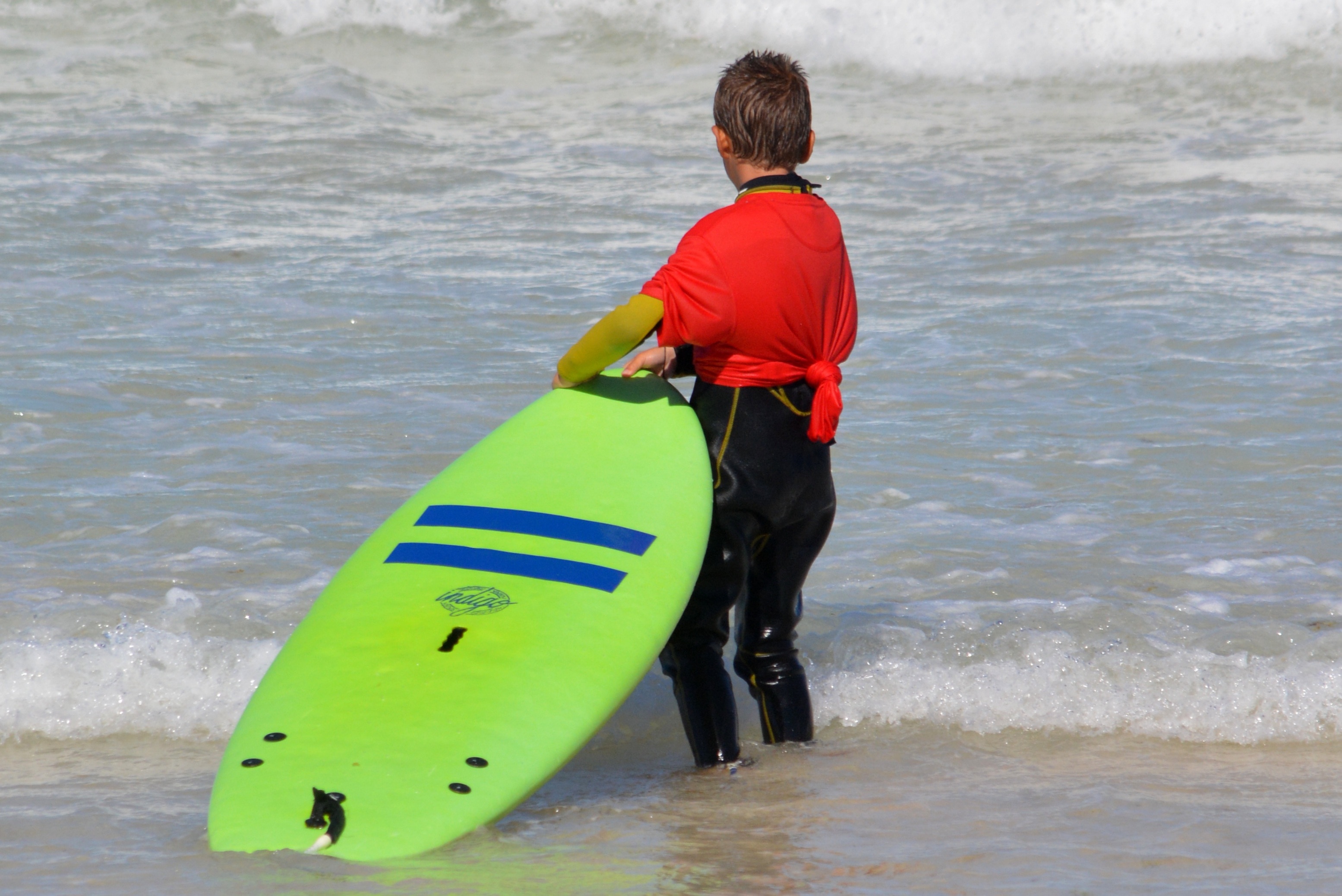 boy holding a green surfboard toward the waves