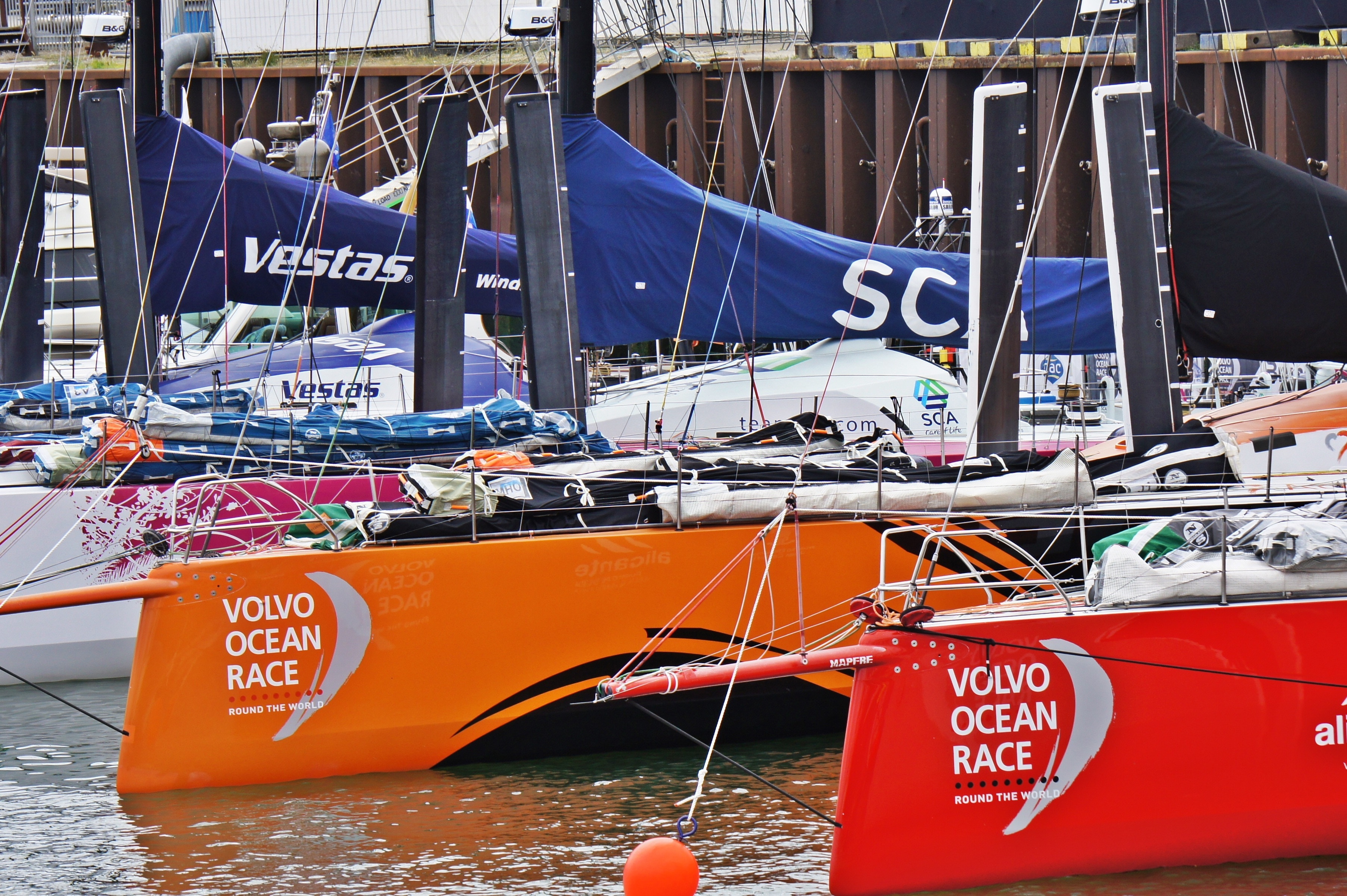 orange and red volvo ocean race boats dock on seaside