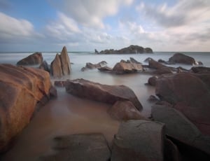 brown rocks on sea water under white cloudy sky thumbnail