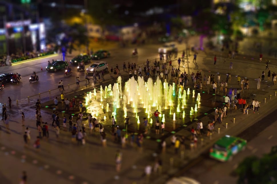 tilt photography of people beside fountain and cars at nigh time preview