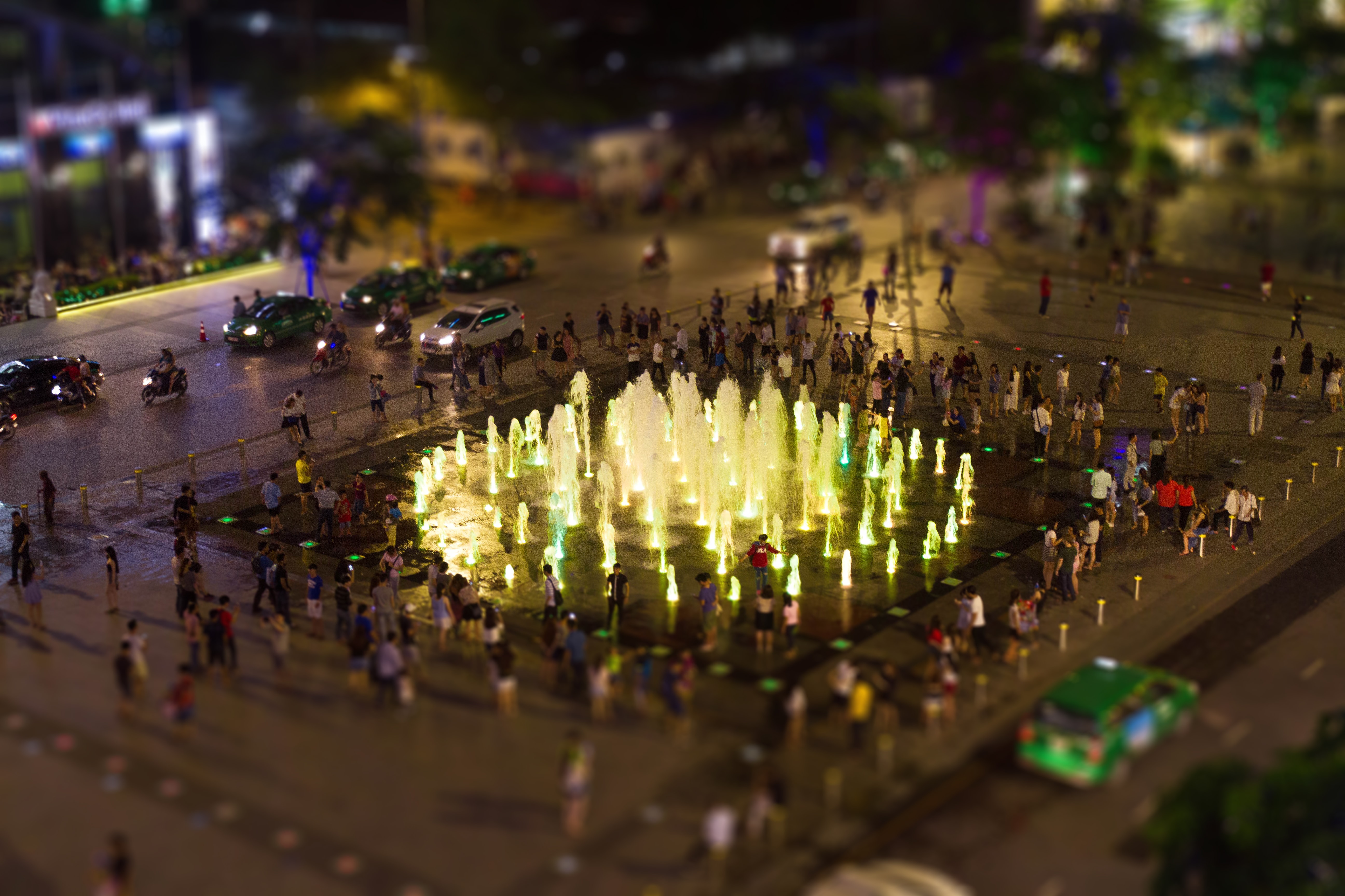 tilt photography of people beside fountain and cars at nigh time