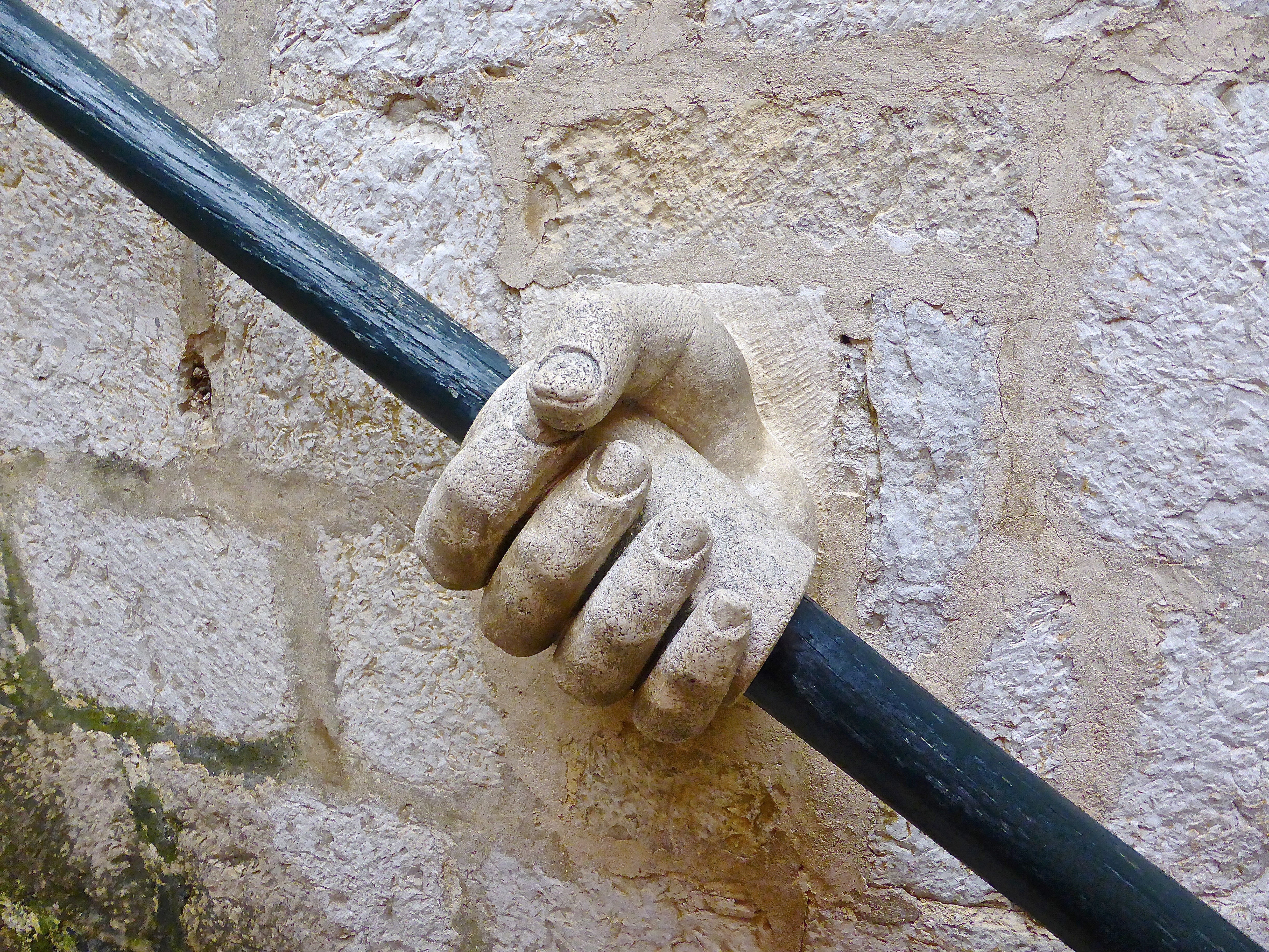 beige concrete hand holding black metal pole