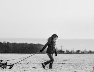 graycale photography of woman pulling child in cart on snow covered ground beside forest thumbnail
