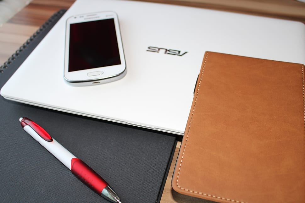 white and red click pen beside brown leather case and white android smartphone on white Asus laptop preview