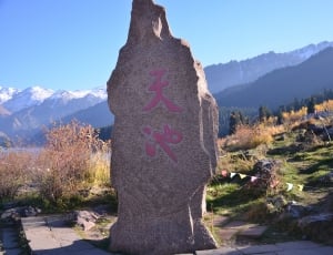 grey stone with pink kanji text surrounded by green grass under clear blue sky thumbnail