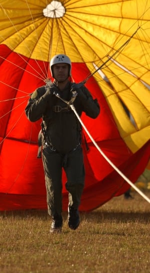 man in brown coveralls and grey helmet holding yellow and red parachute thumbnail