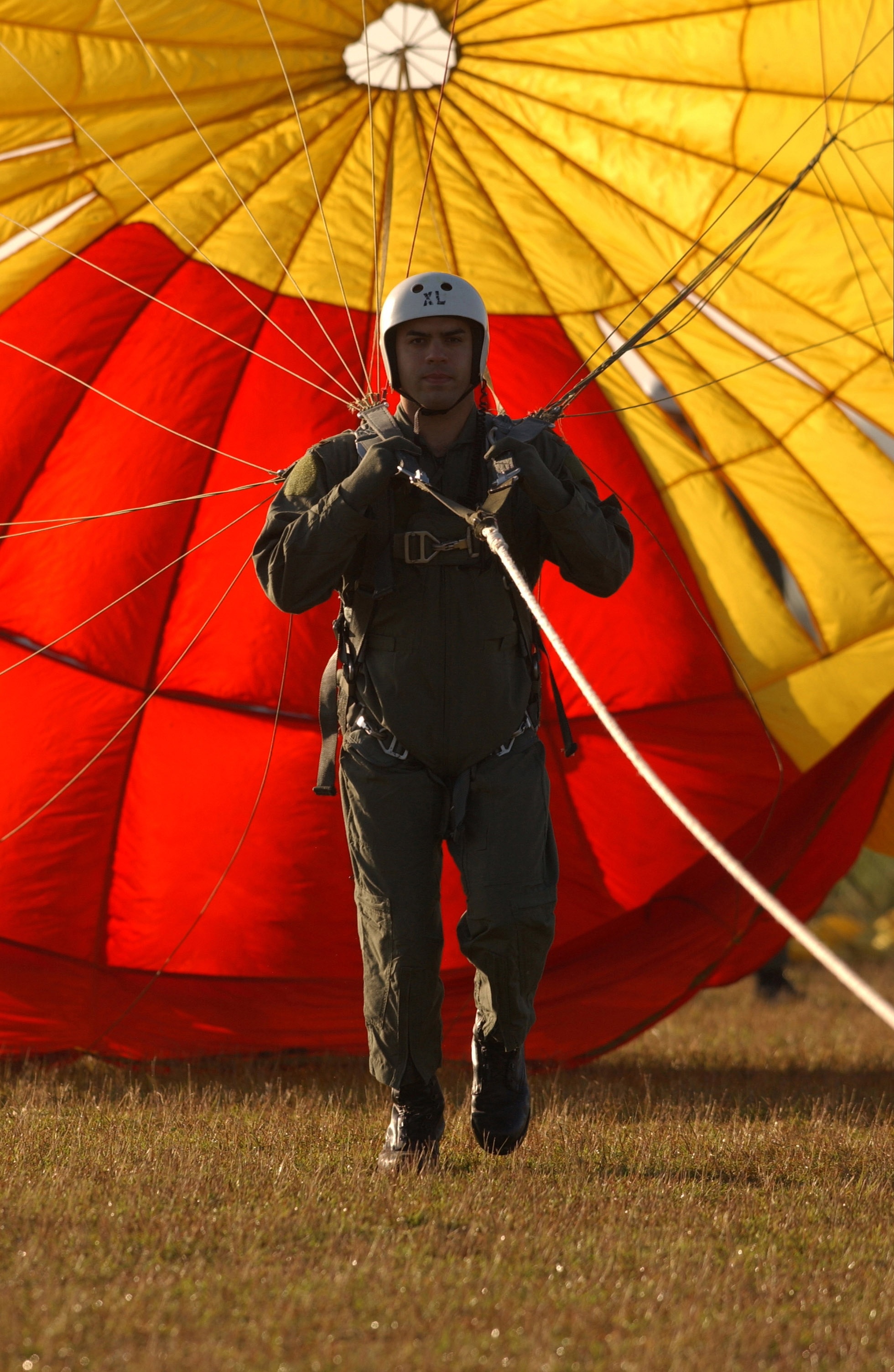 man in brown coveralls and grey helmet holding yellow and red parachute