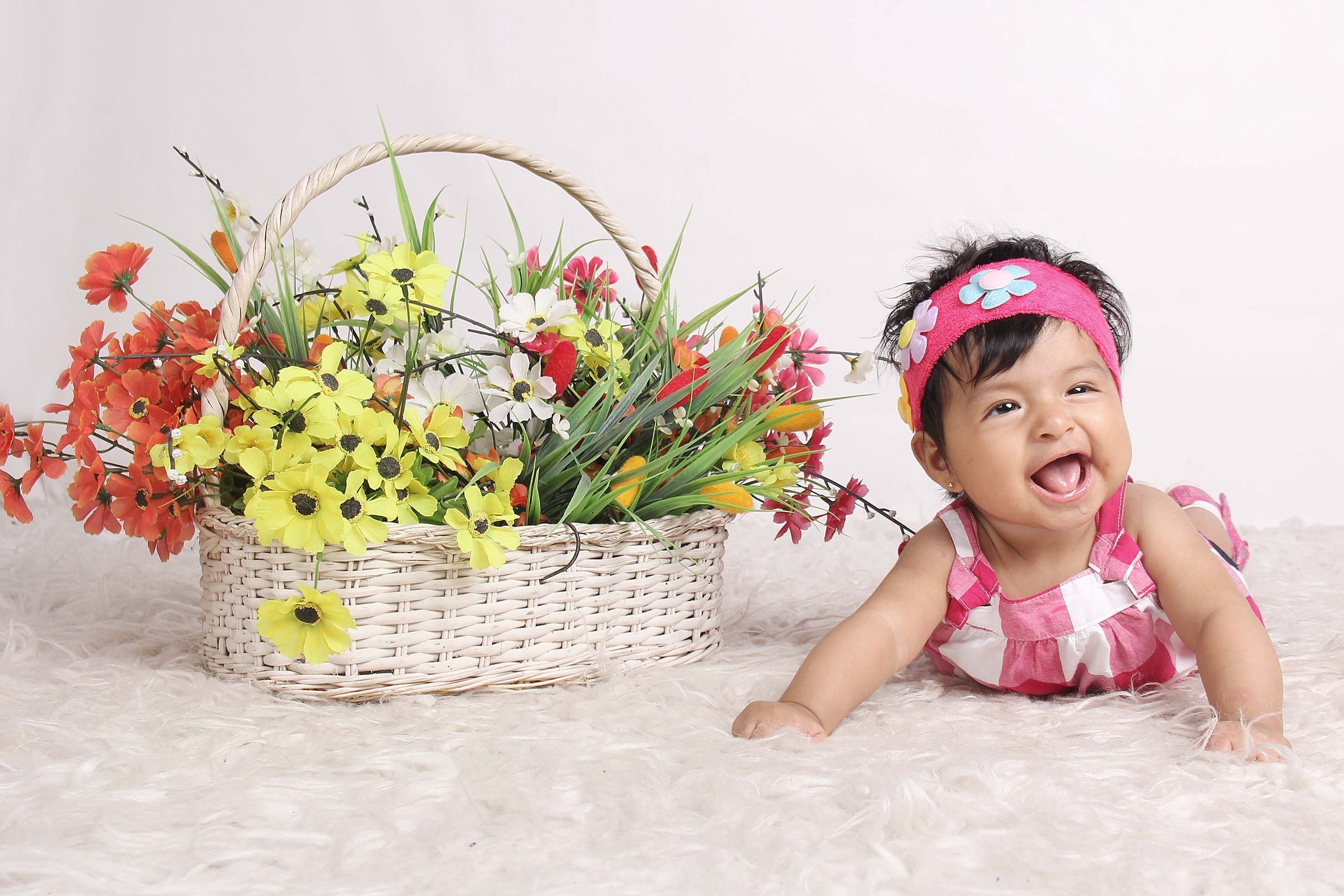 baby in pink and white dress beside basket of cosmos flower