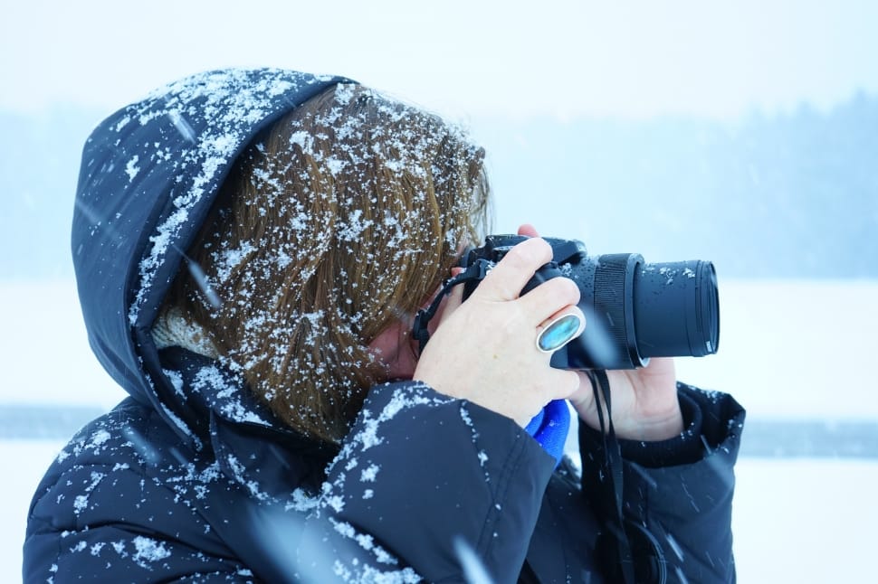 person wearing black snow jacket holding black bridge camera preview