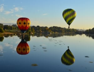 two hot air balloons floating above body of water under clear sky during daytime thumbnail