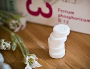 five stacked round white medicinal pills beside white petaled flower thumbnail