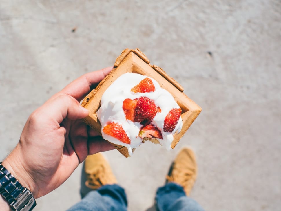 person holding Belgian waffle top with whip cream and strawberries preview