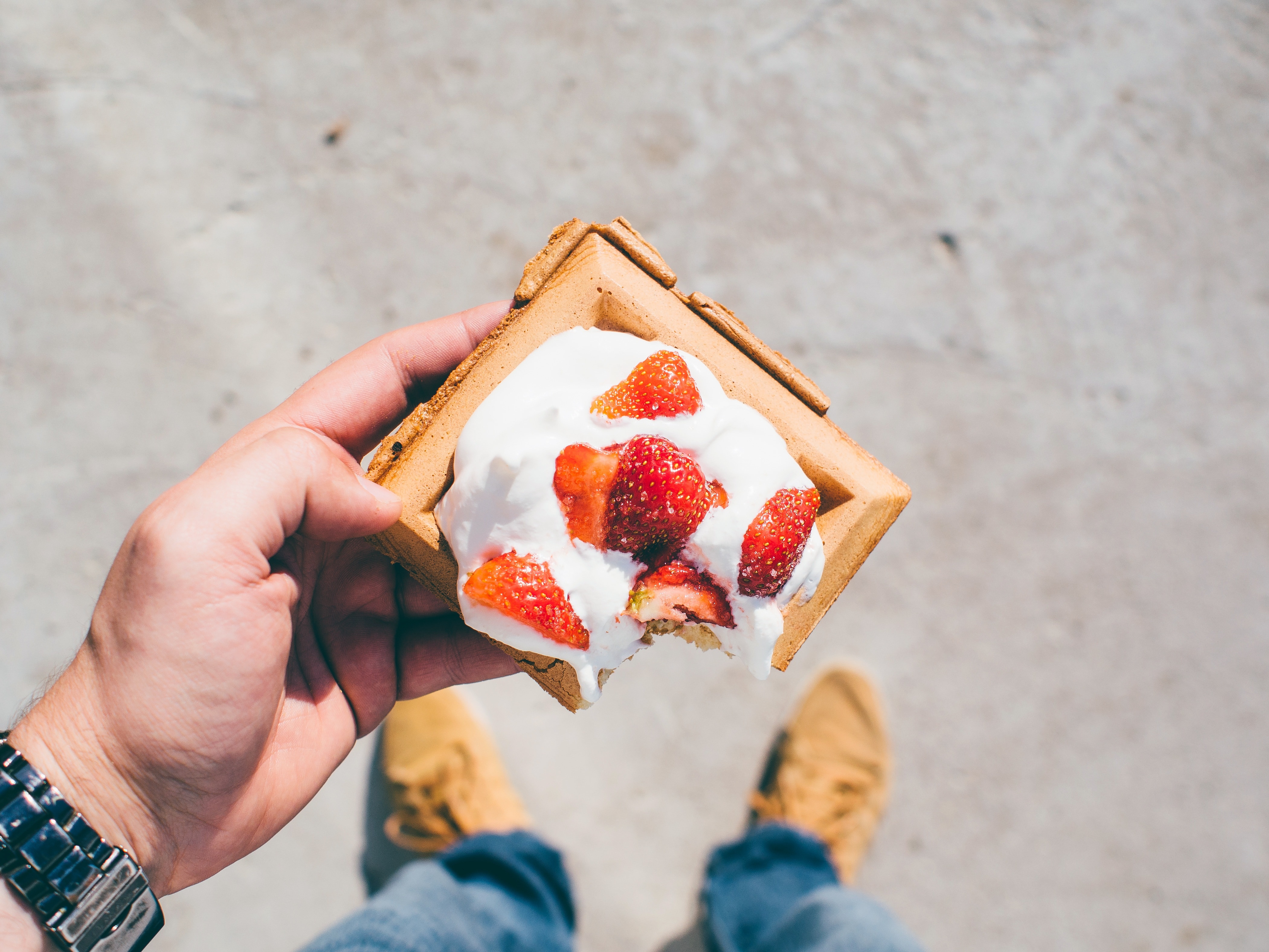 person holding Belgian waffle top with whip cream and strawberries