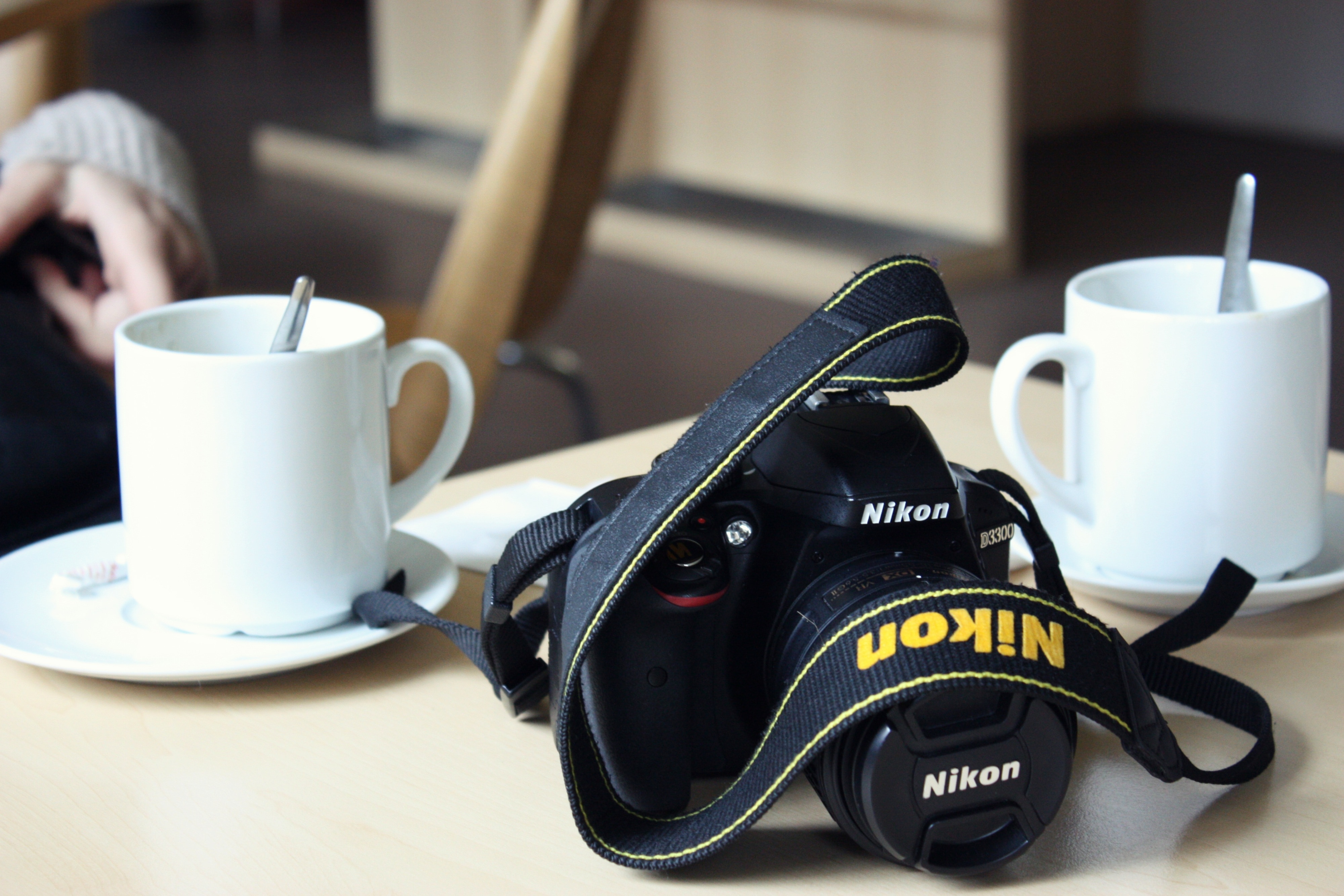 black Nikon DSLR camera with two white ceramic mug in saucers